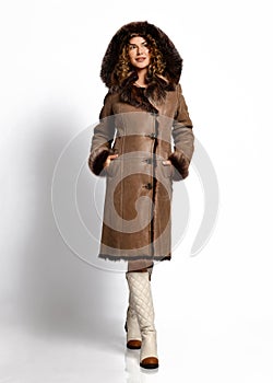 Wealthy woman with long curly red hair in luxury brown sheepskin coat with large fluffy fur hood and cuffs on white