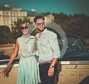 Wealthy young couple near classic convertible against royal palace