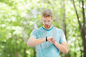 Wearable technology. Handsome athlete using smartwatch technology during training outdoor. Fit athlete tracking his