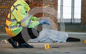 Wearing gloves. Male detective is collecting evidence in a crime scene near dead body on the construction site