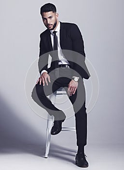 Wearing my best suit. Studio shot of a young man posing against a grey background.