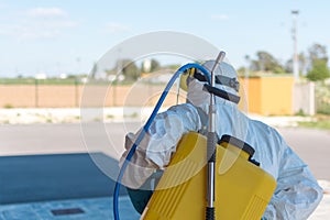 Wearing an NBC personal protective equipment ppe suit, gloves, mask, face shield, cleaning the streets with a backpack of