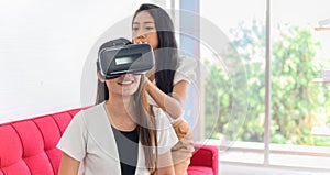 Wearing virtual reality headset for playing online game. Asian woman lifestyle at home with Thai friend.