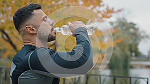 A weary male athlete, soaked in sweat, sips water from a sports bottle after a strenuous jog in a city park, showing