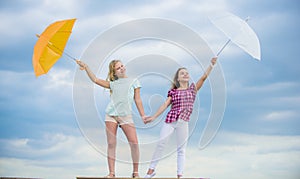 Weather changing. Girls friends with umbrellas cloudy sky background. Carefree children outdoors. Freedom and freshness