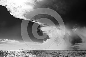Weather changing in the Tropes, upcoming dramatic thunderstorm sky over calm sea with small fishing boat. Black and white photo