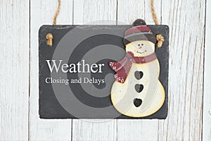 Weather closing and delays sign on a hanging chalkboard with snowman