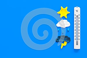 Weather forecast concept. Air temperature. Termometer among cloud and lightening, sun, rainy clouds on blue background