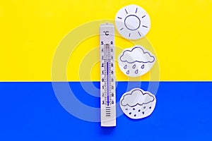 Weather forecast concept. Air temperature. Termometer among cloud, sun, rainy clouds, snow on yellow and blue background