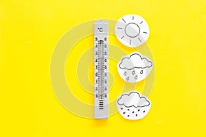Weather forecast concept. Air temperature. Termometer among cloud, sun, rainy clouds, snow on yellow and yellow photo