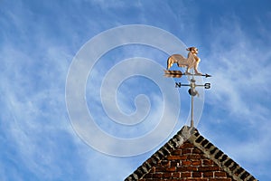 Weathercock also known as weather vane or wind vane on top of old red brick construction against a blue sky photo