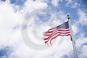 Weathered American flag on a pole with blue sky background. Old flag, flapping in the wind on pole. Fourth of July, Patriotism.