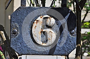 A weathered blue house number plaque, showing the number six