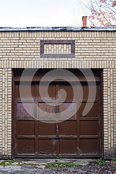 Weathered brown single car residential garage door inset in a light brick wall, creative copy space