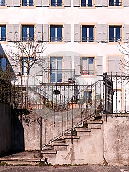 Weathered concrete staircase with wrought iron handrails and facade of building with windows with wooden shutters.