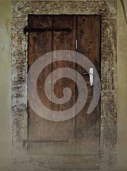 Weathered door made of brown wooden beams with rusty hinges in a massive wall of natural stones