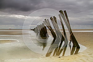 Weathered groynes in sea under dark clouds