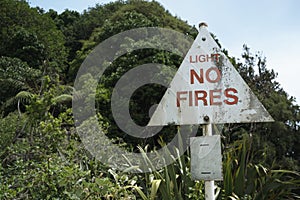 A weathered light no fires red and white warning sign beside a forest.