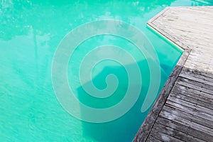 Weathered old wooden terrace of swimming pool deck and freshness turquoise water with natural reflection of environment and shadow