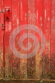 Weathered, red barn door with mud at the base.