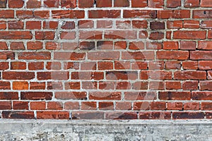 Weathered red brick wall with damages and missing joints on a grey concrete socket, use as game asset texture or reference image