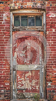 A weathered red door set in an old brick wall tells a story of the past. The contrasting textures and colors speak