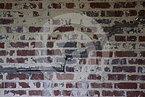 Weathered red, white, and black brick wall with diagonal crack