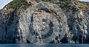 Weathered seaside rock face texture with parts of green and blue water. Aged volcanic stone wall surface background