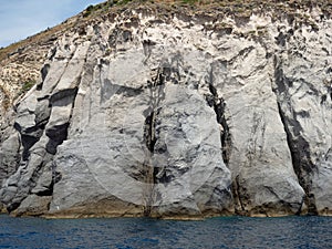 Weathered seaside rock face texture with parts of green and blue water. Aged volcanic stone wall surface background