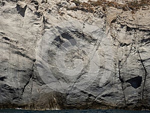 Weathered seaside rock face texture with parts of green and blue water. Aged volcanic stone wall surface background pattern