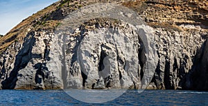 Weathered seaside rock face texture with parts of green and blue water. Aged volcanic stone wall surface background