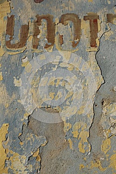 Weathered wall with white,red, blue where the paint is pealing off and red letters