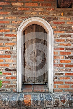 Weathered wooden door with arched top set in colorful red brick wall