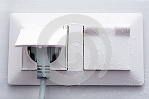 Weatherproof socket on a white tiled wall with water droplets