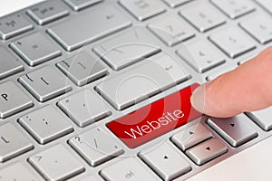 Web design concept: a finger press red website button on laptop keyboard