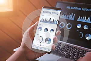 Web Marketing management and reports background concept. Close-up rear view of a person  holding and looking at smartphone and