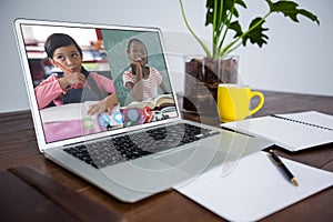 Webcam view of two female students on video conference on laptop on wooden table