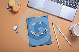 Webinar text from wooden letters on notepad on desktop with laptop and coffee on colored background. Top view, flat lay