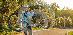 Website header of Strong athletic man in sportswear holding a bicycle while standing in park at sunset, cycling outdoors