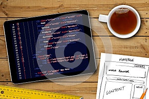 Website wireframe sketch and programming code on digital tablet