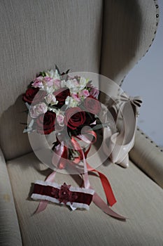 A bride`s bouquet of red and pink roses, women`s shoes, a garter of the bride