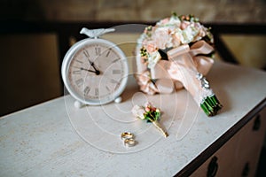 Wedding accessories. Boutonniere, Golden rings, a beautiful bouquet of flowers on white textured table. Concept of bride
