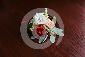 Wedding accessories of the budo of red, white and pink flowers for the groom with a ring on a dark wooden background