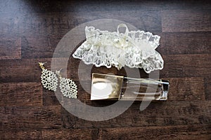 Wedding accessories. Gold perfume, bridal earrings with gemstones and white garter.