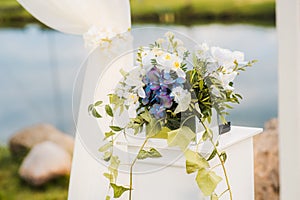 The wedding arch is decorated with blue flowers and white light silk. Summer ceremony. Bridal bouquet