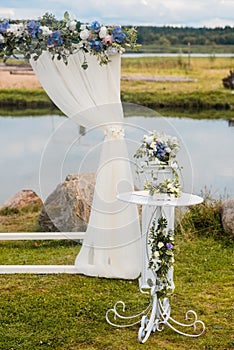 The wedding arch is decorated with blue flowers and white light silk. Summer Wedding Ceremony