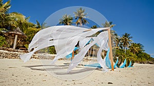 Wedding arch decorated with flowers on the beach near the ocean. Her white and blue canvases fly in the wind. Decorative