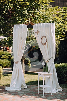 Wedding arch decorated with white cloth curtains, frame and white curbstone with bottles