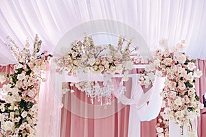 Wedding arch decorated with white and pink cloth, crystal chandelier and beautiful floral compositions of roses and ranunculus