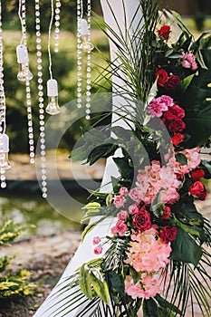 Wedding arch decoration close-up. Flower bouquets of palm leaves, pink and red roses, light bulbs and crystals